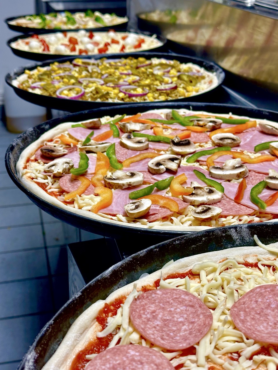 Mehrere frisch belegte Pizzen vor dem Backen